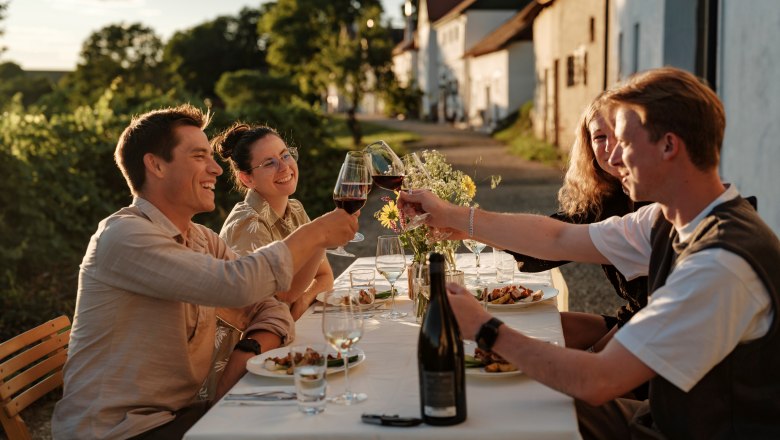 Weinviertler Kellergassenkulinarium, © Weinstraße Weinviertel / Reidinger Gruppe von Menschen stößt bei einem Essen im Freien mit Weingläsern an.