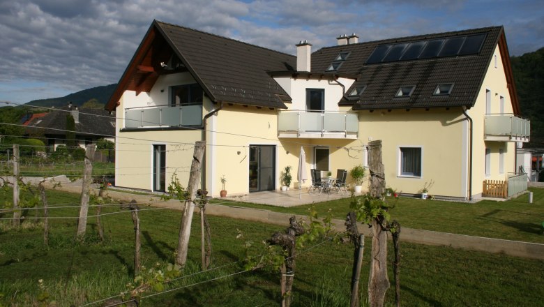 Gästezimmer Auer, © Gerhard Auer Gelbes Haus mit Balkon und Garten, umgeben von Weinreben.