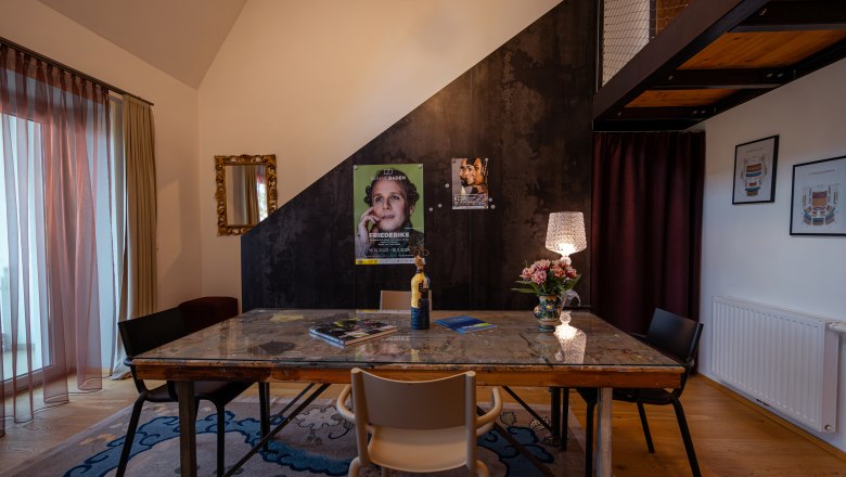 At the Park Hotel, © Niederösterreich Werbung / Maximilian Pawlikowsky Ein stilvoll eingerichteter Raum mit einem Tisch, Stühlen, einer Lampe und Postern an der Wand.
