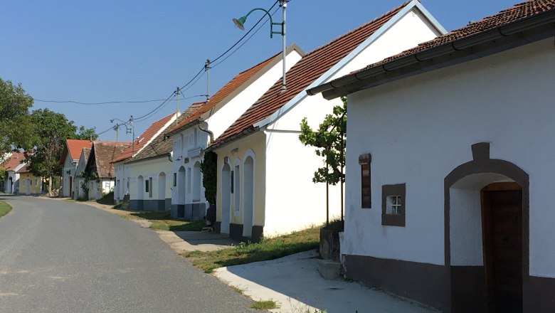 Kellergasse Niederschleinz, © Marktgemeinde Sitzendorf Eine ruhige Straße mit traditionellen, weiß getünchten Häusern und roten Dächern in einer ländlichen Umgebung.