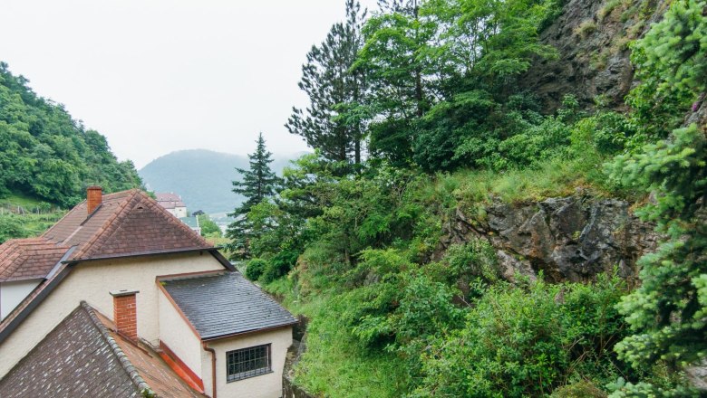 Ausblick von der Terrasse, © Gästezimmer Rolea Blick von einer Terrasse auf ein Hausdach, umgeben von grünen Bäumen und Felsen.