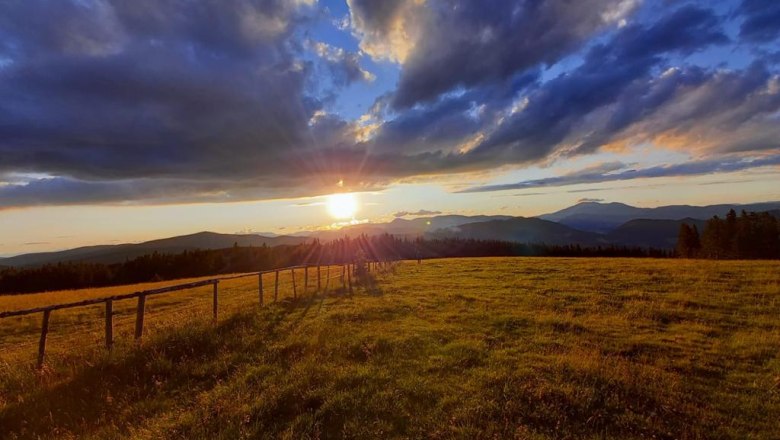 Sonnenuntergang Feistritzer Schwaig, © Heinz Brandl Sonnenuntergang über einer grünen Wiese mit Bergen im Hintergrund und dramatischen Wolken am Himmel.