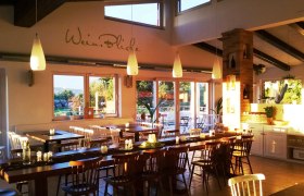 Gastzimmer Müllner Tom, © Helge Wöll Ein gemütliches Gastzimmer mit Holztischen und Stühlen, dekoriert mit Kerzen und Pflanzen, beleuchtet von warmem Sonnenlicht.