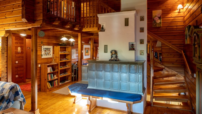 Salomons Eulennest, © Imre Antal Gemütliches Wohnzimmer aus Holz mit Kachelofen und Treppe.