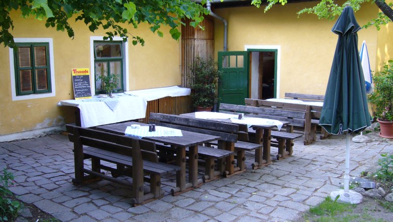 Innenhof Gasthaus Perzy, © Gemeinde Haugschlag Innenhof eines Gasthauses mit Holzbänken und Tischen, gelbe Wand, grüner Tür und Fenster, Sonnenschirm und Pflanzen.