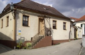 Haus, © Thomas Schmelz Ein kleines, älteres Haus mit braunem Dach und Treppe in einer ruhigen Straße.