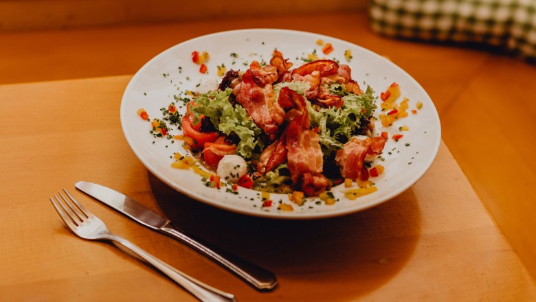 "Salathaufen" mit Ziegenkäse aus der Buckligen Welt, © Niederösterreich Werbung/Klaus Engelmayer Ein Teller mit gemischtem Salat, Ziegenkäse und Speck auf einem Holztisch.