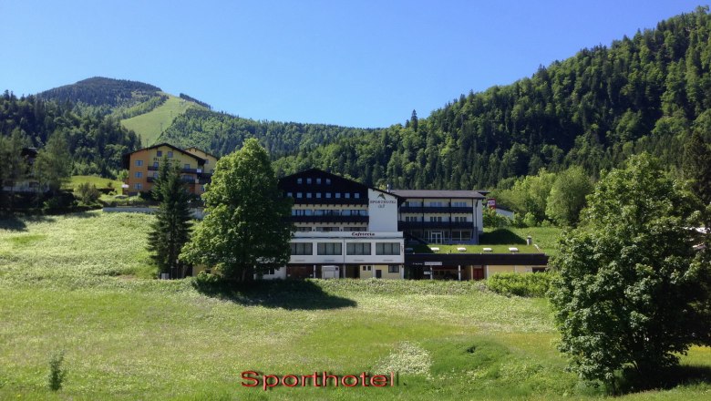 Sporthotel am Ötscher, © zVg Ein Sporthotel in einer grünen Berglandschaft mit blauem Himmel.