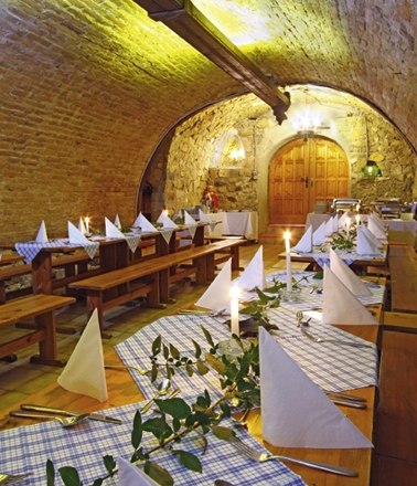 Bacchuskeller, © Bauer & CO Ges.m.b.H. Ein rustikaler Weinkeller mit langen Holztischen, blau-weiß karierten Tischdecken und Kerzenbeleuchtung.