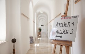 Atelier, © akademie.Geras2011 Ein heller Flur mit einem Schild auf einer Staffelei, das auf Atelier 1 und Atelier 2 hinweist.