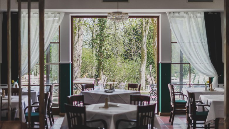 Gastraum, © Schlossschenke Ein Restaurant mit gedeckten Tischen und Blick auf einen grünen Garten durch große Fenster.