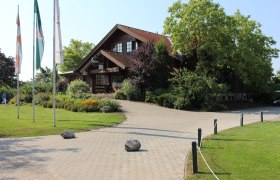 Golfclub Schönfeld, © Gemeinde Lassee Eingang eines Golfclubs mit Holzgebäude und Fahnen.