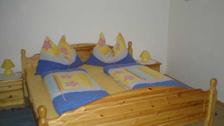 Zimmer, © Schwarzinger Holzbett mit bunter Bettwäsche in einem Schlafzimmer.