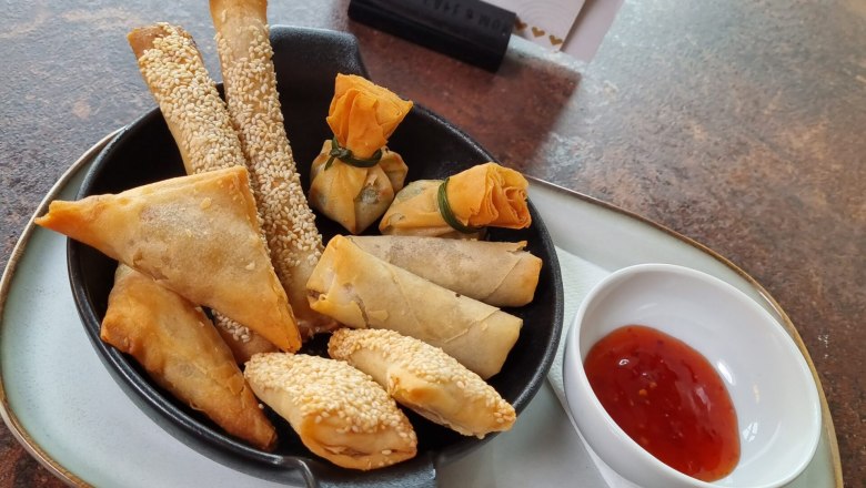 Cafe Herzstück, © Cafe Herzstück_Stephanie Kirschner Verschiedene frittierte Snacks auf einem Teller mit Dip und Café Herzstück Menü im Hintergrund.