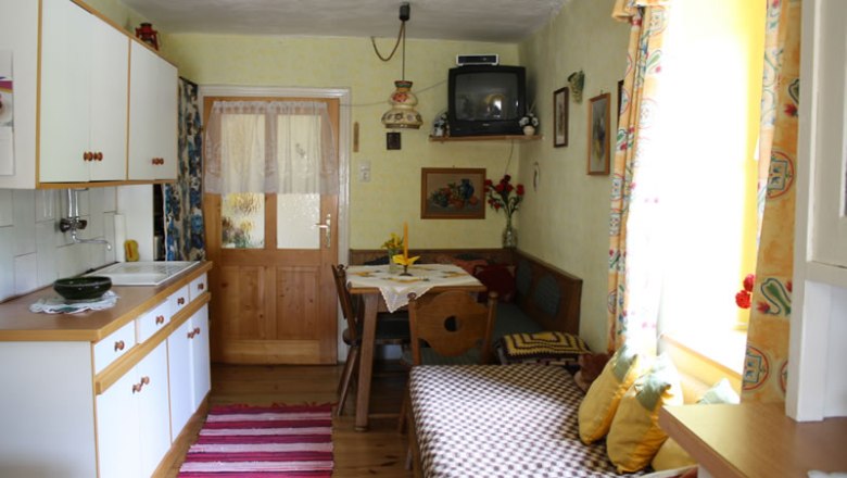 Küche in der Ferienwohnung, © Jamek Gemütliche Küche in einer Ferienwohnung mit Holzmöbeln, kleinem Esstisch und Fernseher.