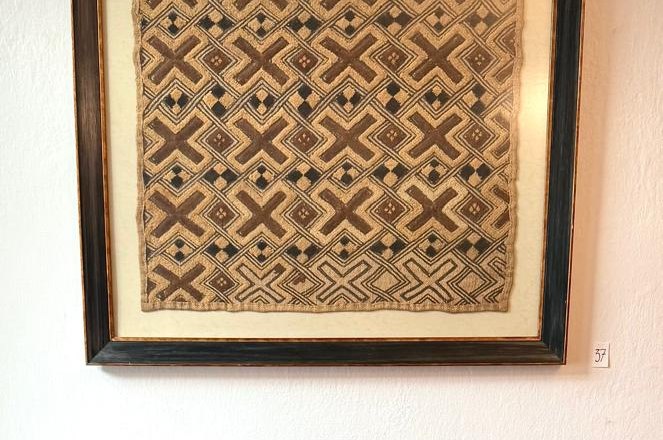 die Galerie MERKIMA, © Doris Hauser Rotes Sofa vor einem gerahmten, gemusterten Kunstwerk an der Wand.