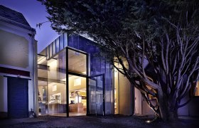 Außenansicht, © Andreas Schleissinger Moderne Glasfassade eines Gebäudes bei Nacht, umgeben von Bäumen.