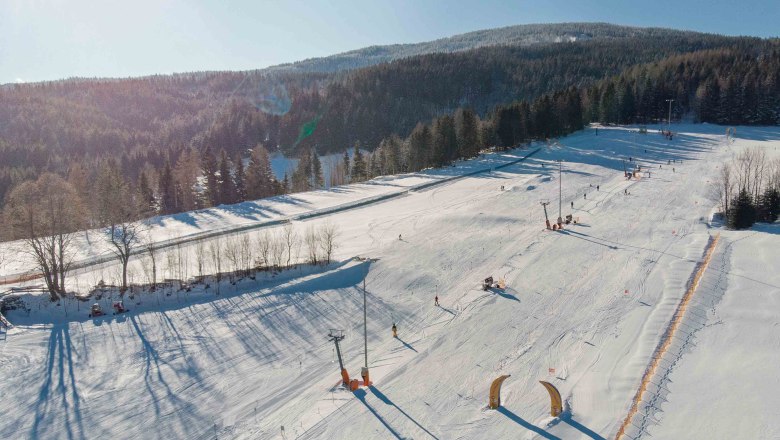 Familienskiland der Wexl Arena St. Corona am Wechsel, © Wexl Arena St. Corona am Wechsel Luftaufnahme eines verschneiten Skigebiets mit Pisten und Wald im Hintergrund.