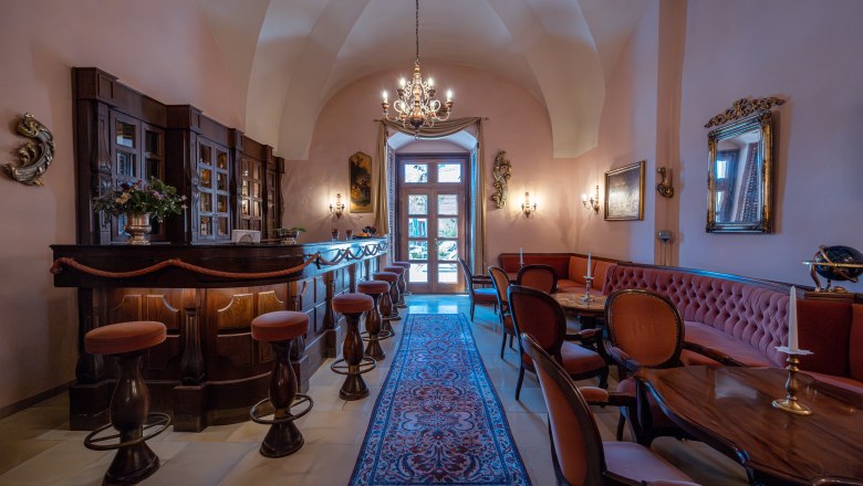 Hotel Schloss Dürnstein, © Niederösterreich Werbung / Maximilian Pawlikowsky Eleganter Innenraum einer Hotelbar mit Holzmöbeln, Kronleuchter und Teppich.