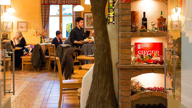 Innenansicht Heurigenlokal, © Der Baumgartner Innenansicht eines Heurigenlokals mit Baumdeko und Weinregal.