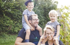 TDR-Familienfoto, © Buschenschank Buder Familie im Freien, zwei Erwachsene tragen Kinder auf den Schultern, sonniger Tag.