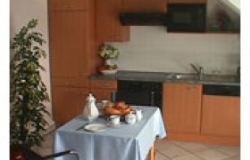 Appartement, © © Fam Pekarek Kleine Küche mit Holzmöbeln, Esstisch mit blauer Tischdecke und Geschirr.