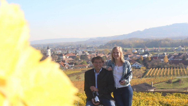 Familie Mittelbach im Weingarten, © Weingut Mittelbach Zwei Personen in einem Weingarten mit Blick auf ein Dorf im Hintergrund.