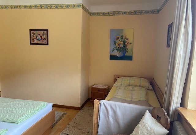 Doppelzimmer kann auch als Dreibettzimmer genutzt werden, © Wiener Alpen Ein Zimmer mit zwei Betten, einem Einzelbett und einem Doppelbett, dekoriert mit Blumenbildern an den Wänden.