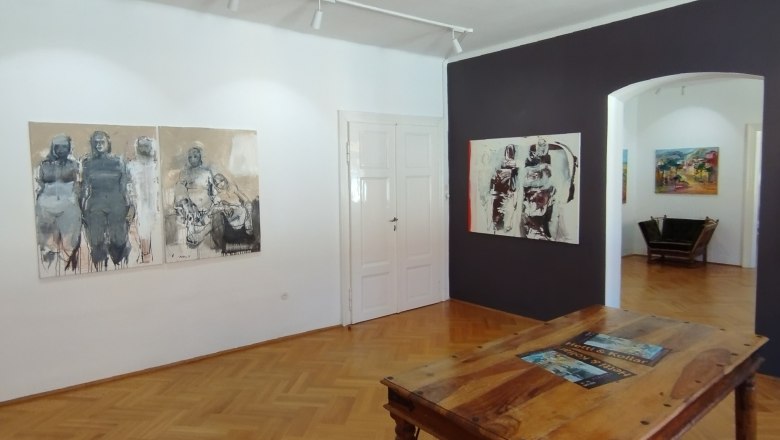 die Galerie MERKIMA, © Doris Hauser Innenansicht einer Kunstgalerie mit Holzboden, Gemälden an den Wänden und einem Holztisch in der Mitte.