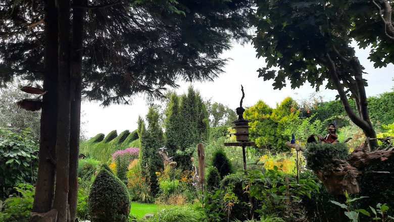 GrünTon Cottage 2024 c_Kralovec, © I.Kralovec Ein üppiger Garten mit Bäumen, Sträuchern und einer Vogelstatue.
