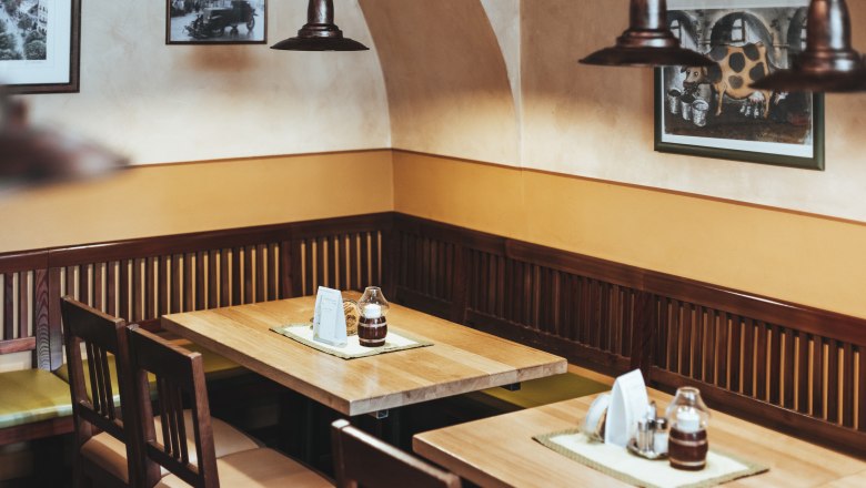 Einkehren in Tulln, © Niederösterreich Werbung/David Schreiber Gemütliche Sitzecke in einem Restaurant mit Holztischen und -stühlen, dekoriert mit Bildern an der Wand.
