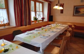 Gasthaus Schönau, © zVg Ein festlich gedeckter Tisch in einem Gasthaus mit weißen Tischdecken, Kerzen und Blumen. Holzmöbel und Fenster mit Vorhängen im Hintergrund.