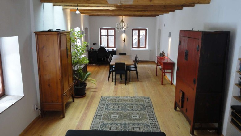 Gillausklause 3, © Stephanus Domanig Ein stilvoll eingerichteter Raum mit Holzboden, Holzbalkendecke, antiken Möbeln und einem Teppich.