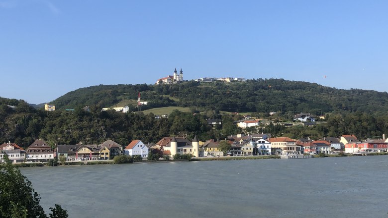 Anlegestelle Krummnussbaum gegenüber der Basilika Maria Taferl, © Donau NÖ Tourismus Blick auf die Basilika Maria Taferl auf einem Hügel, mit Häusern und einem Fluss im Vordergrund.