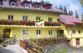 Gasthaus Luf, © Gasthaus Luf, Foto Uno GmbH Gelbes Gasthaus mit roten Dächern und blühenden Blumen auf dem Balkon.