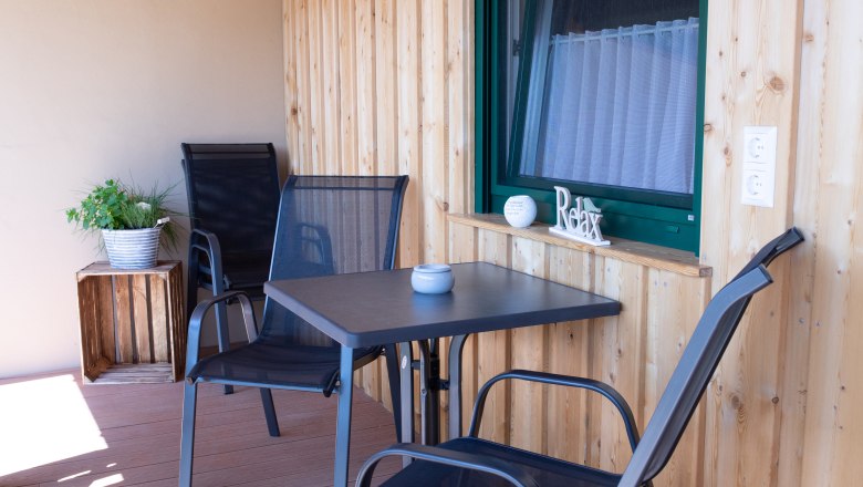 Balkon für gemütliches Verweilen, © Familie Schwalm Ein Balkon mit Holzwänden, zwei schwarzen Stühlen, einem Tisch und einer Pflanze in einem Topf.