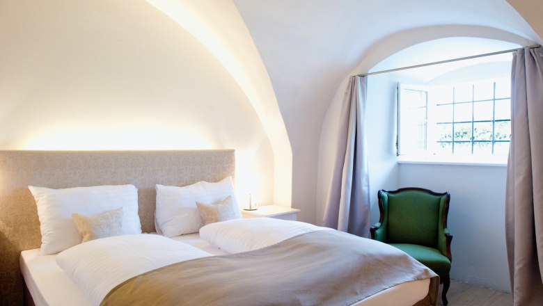 Freigut Thallern, © Freigut Thallern Gemütliches Schlafzimmer mit Doppelbett, grünem Sessel und gewölbter Decke.