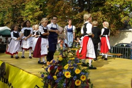 Kinder-Sing- und Volkstanzgruppe Tattendorf, © Gemeinde Tattendorf Kinder in Trachten tanzen auf einer Bühne im Freien.