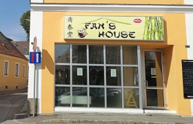 fanshouse_gars, © Roman Zöchlinger Außenansicht eines Restaurants namens Fan's House mit gelber Fassade und großen Fenstern.