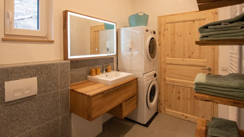 Badezimmer, © Silbersberg Cottage Modernes Badezimmer mit Holzwaschtisch, beleuchtetem Spiegel, Waschmaschine und Trockner. Handtücher auf Holzregalen.