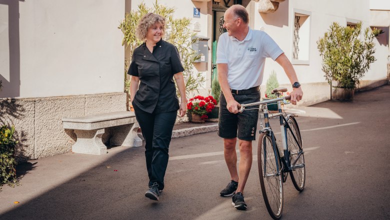 Wirtsleute Gabriele und Gerhard Engel, © Niederösterreich Werbung/Daniela Führer Zwei Personen unterhalten sich, während einer ein Fahrrad schiebt.