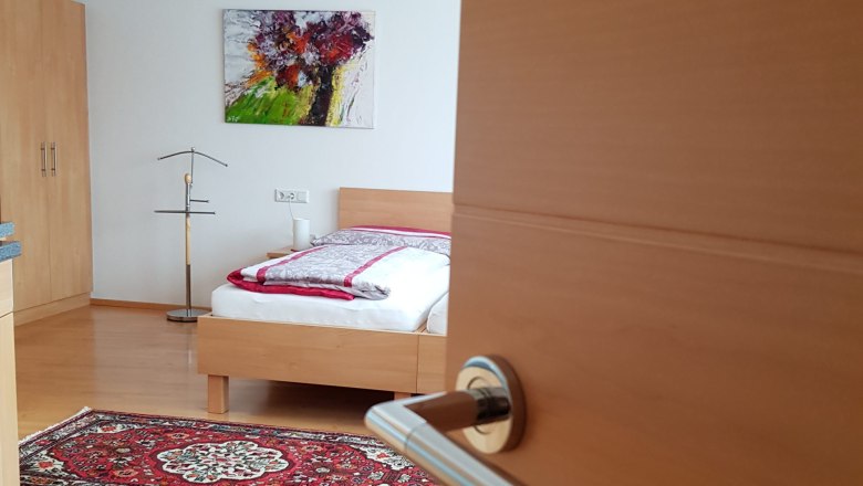 Doppelzimmer, © BIO-Weingut Poys Ein geöffnetes Zimmer mit einem Bett, Teppichen und einem Gemälde an der Wand.