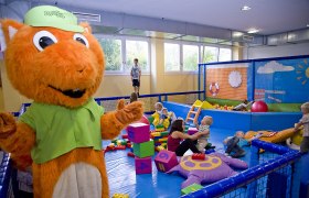 kids space Kleinkinderbereich, © kids space gars Kinder spielen in einem Indoor-Spielbereich mit einem großen orangefarbenen Maskottchen.