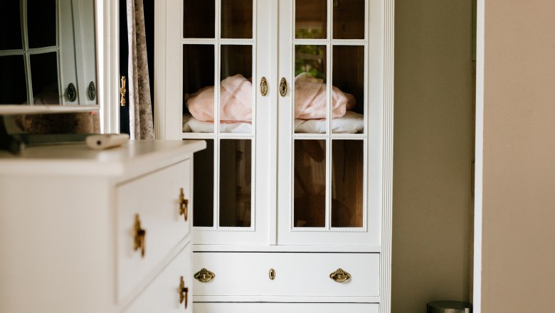 villa_schonthal-13_4, © Julius Hirtzberger Weißer Schrank mit Glastüren und Schubladen, daneben eine Kommode und ein Mülleimer.