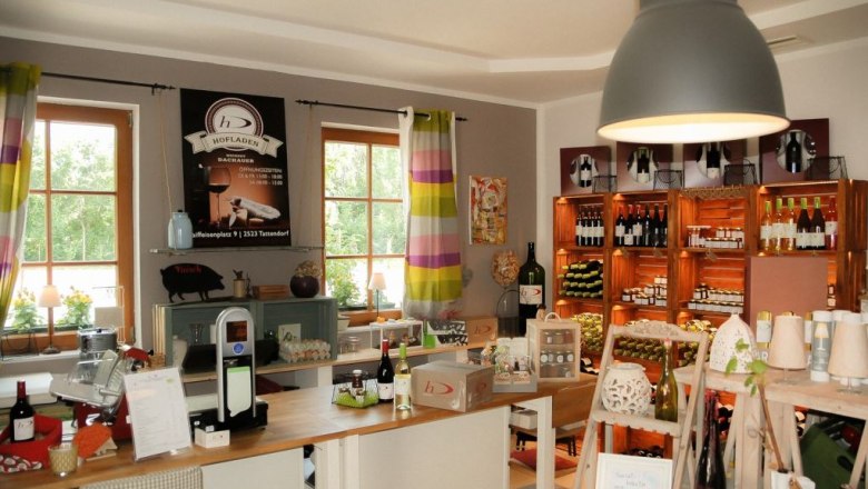 Der Hofladen, © Weingut Dachauer Innenansicht eines Hofladens mit Regalen voller Weinflaschen und Produkten.