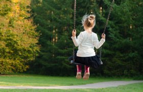 Spielplatz, © pixabay Ein Kind schaukelt in einem Park, umgeben von grünen Bäumen.