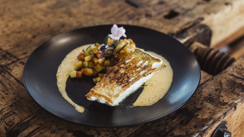 Gehobene, traditionelle Küche von höchster Qualität, © Niederösterreich Werbung/David Schreiber Gebratener Fisch mit Gemüsewürfeln und Sauce auf schwarzem Teller serviert.