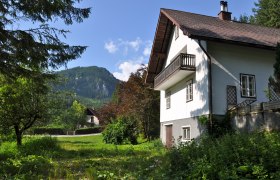 Ferienhaus Erlaufboden, © zVg Gemeinde Annaberg Ein weißes Ferienhaus mit Balkon vor einer Berglandschaft und grünem Garten.