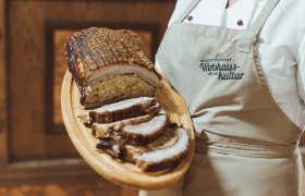 Gefüllte Brust vom Duroc-Schwein, © Niederösterreich Werbung/David Schreiber Gefüllte Schweinebrust auf Holzplatte, serviert von Person in Schürze.