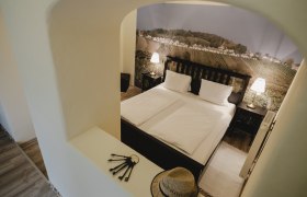 Weinviertel Zimmer, © Michael Reidinger Ein gemütliches Schlafzimmer mit Doppelbett, zwei Nachttischlampen und einer Wandtapete mit Weinlandschaft.